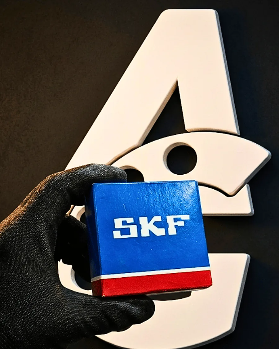 Mano con guante sosteniendo una caja azul y roja de rodamientos SKF frente al isotipo de Arcaragua Group